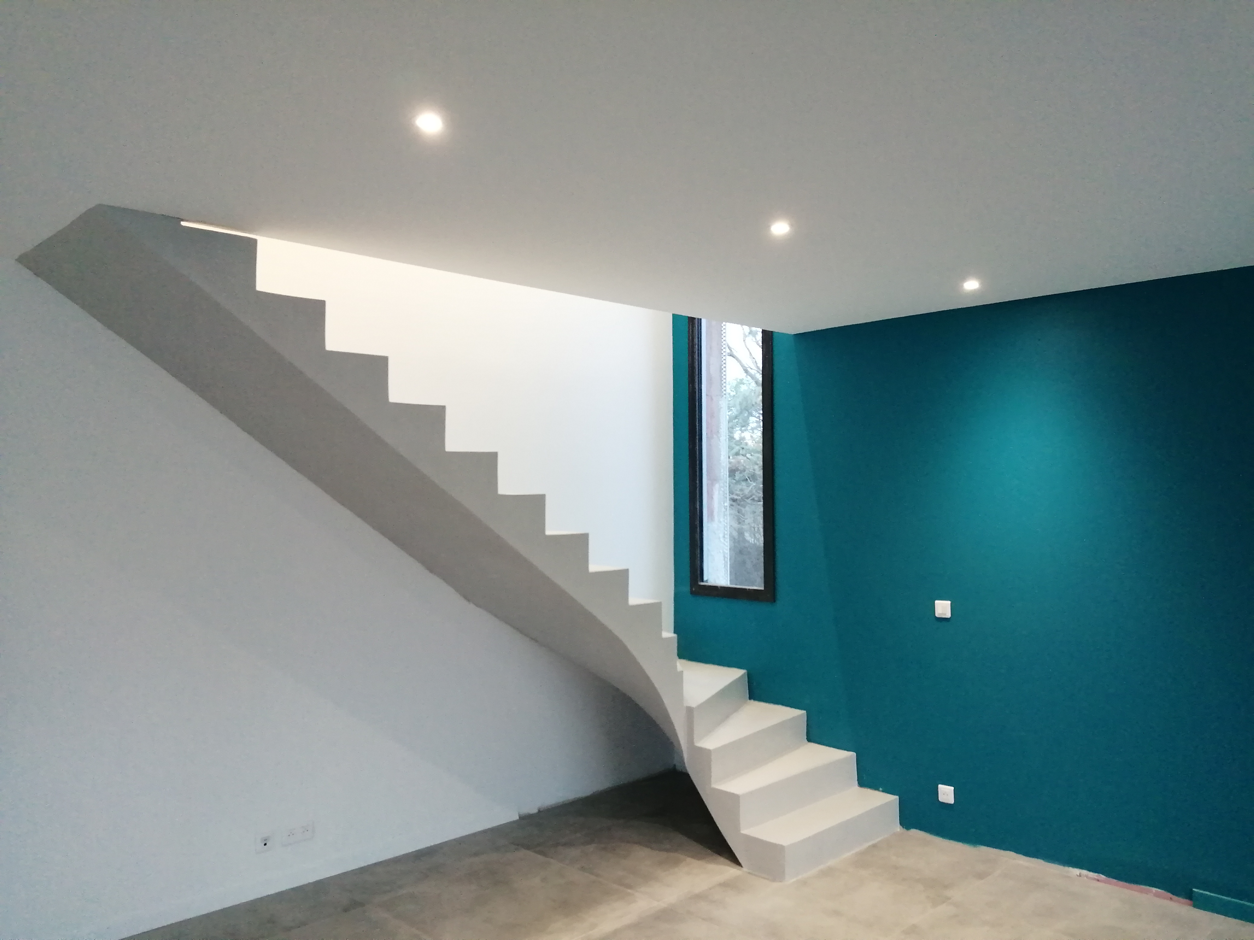 Escalier en béton ciré dans un salon sur fond d'un mur en bleu turquoise.