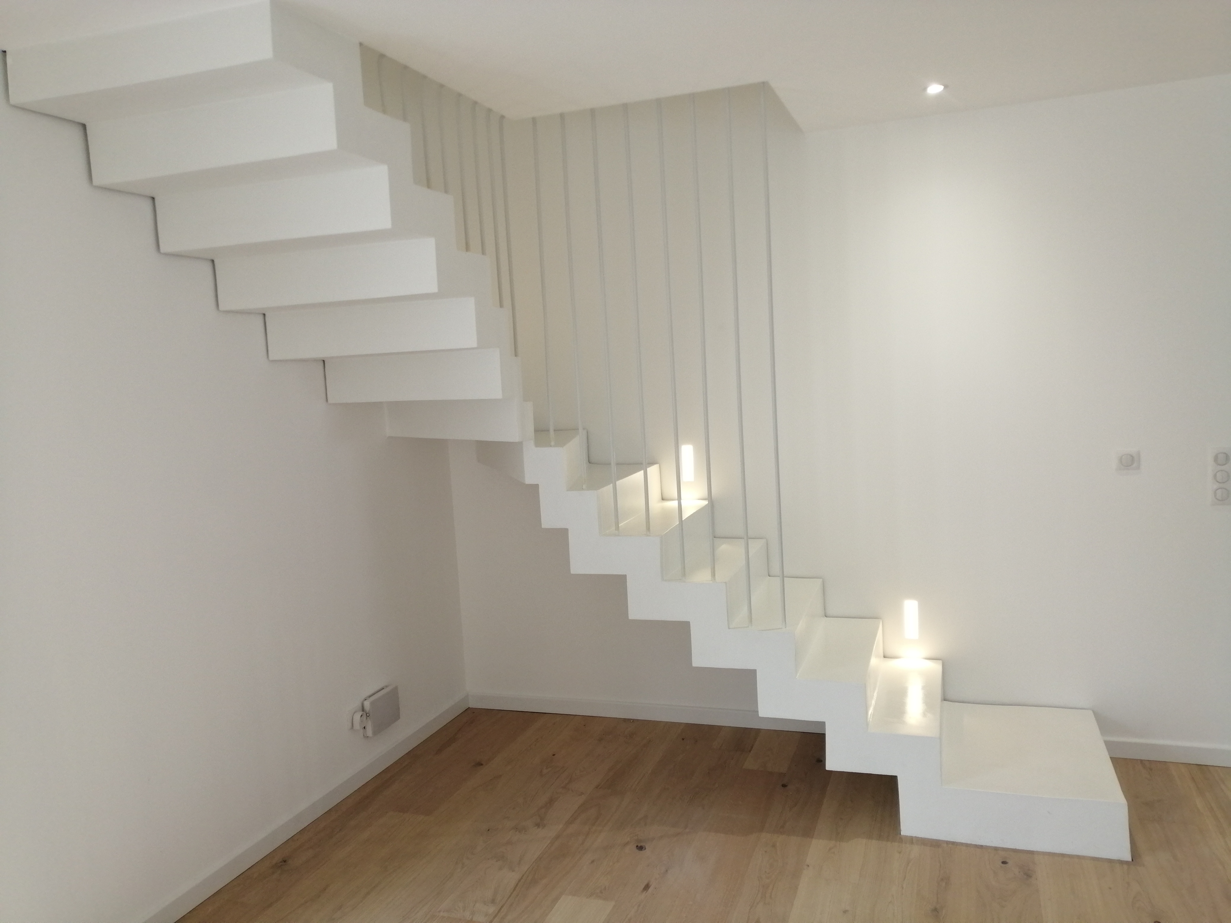 Application d'un béton ciré blanc pur sur un escalier béton un quart balancé avec une première marche palière