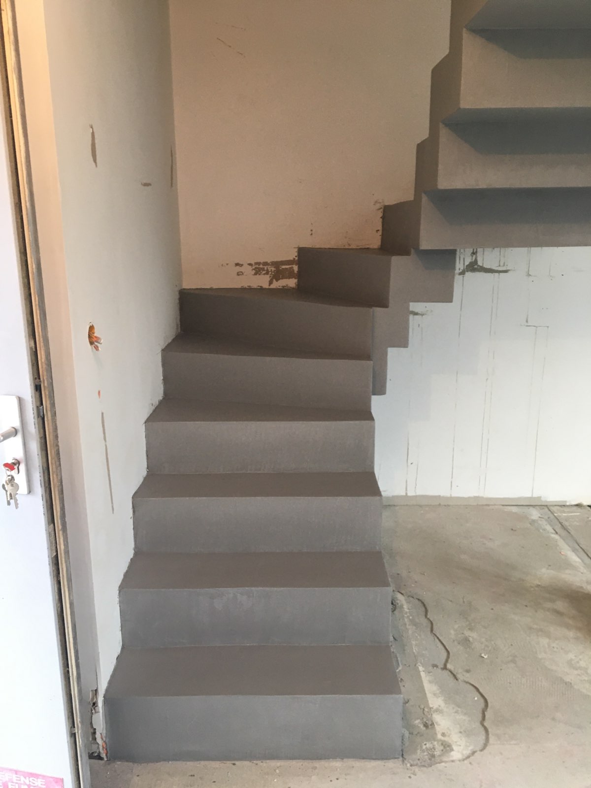 Revêtement en béton ciré couleur Argent pour cet escalier dans une villa en rénovation. Escalier unique par un design crémaillère et un mélange d'un balancé couplé à un palier intermédiaire.